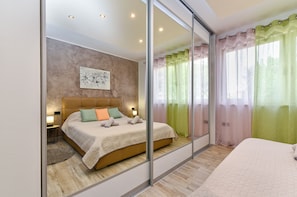 Un dormitorio moderno con una cama grande, una mesita de noche con lámpara, una obra de arte en la pared y un puerta corrediza de vidrio que da a un balcón.