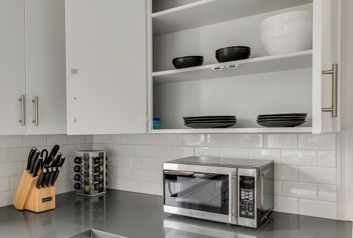 Une cuisine avec des meubles blancs, un four à micro-ondes et un bloc à couteaux.