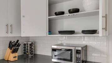 Une cuisine avec des meubles blancs, un four à micro-ondes et un bloc à couteaux.
