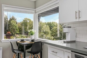 Eine Küche mit weißen Schränken, einer Kaffeemaschine und Blick auf Grünflächen.