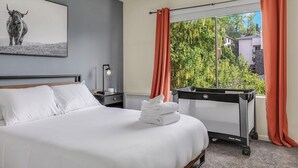 Et hotelværelse med en seng, et billede af en tyr på væggen, et vindue med orange gardiner og en radiator.
