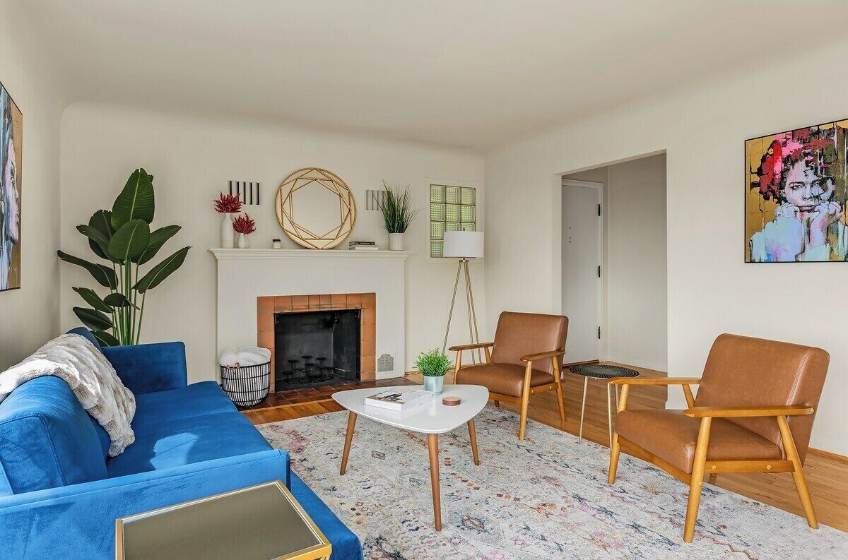 A living room with a blue sofa, two brown chairs, a white coffee table, a fireplace, and a large plant.