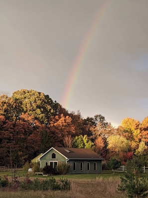 A green house with a sloped roof, surrounded by a grassy field and trees with autumn foliage.