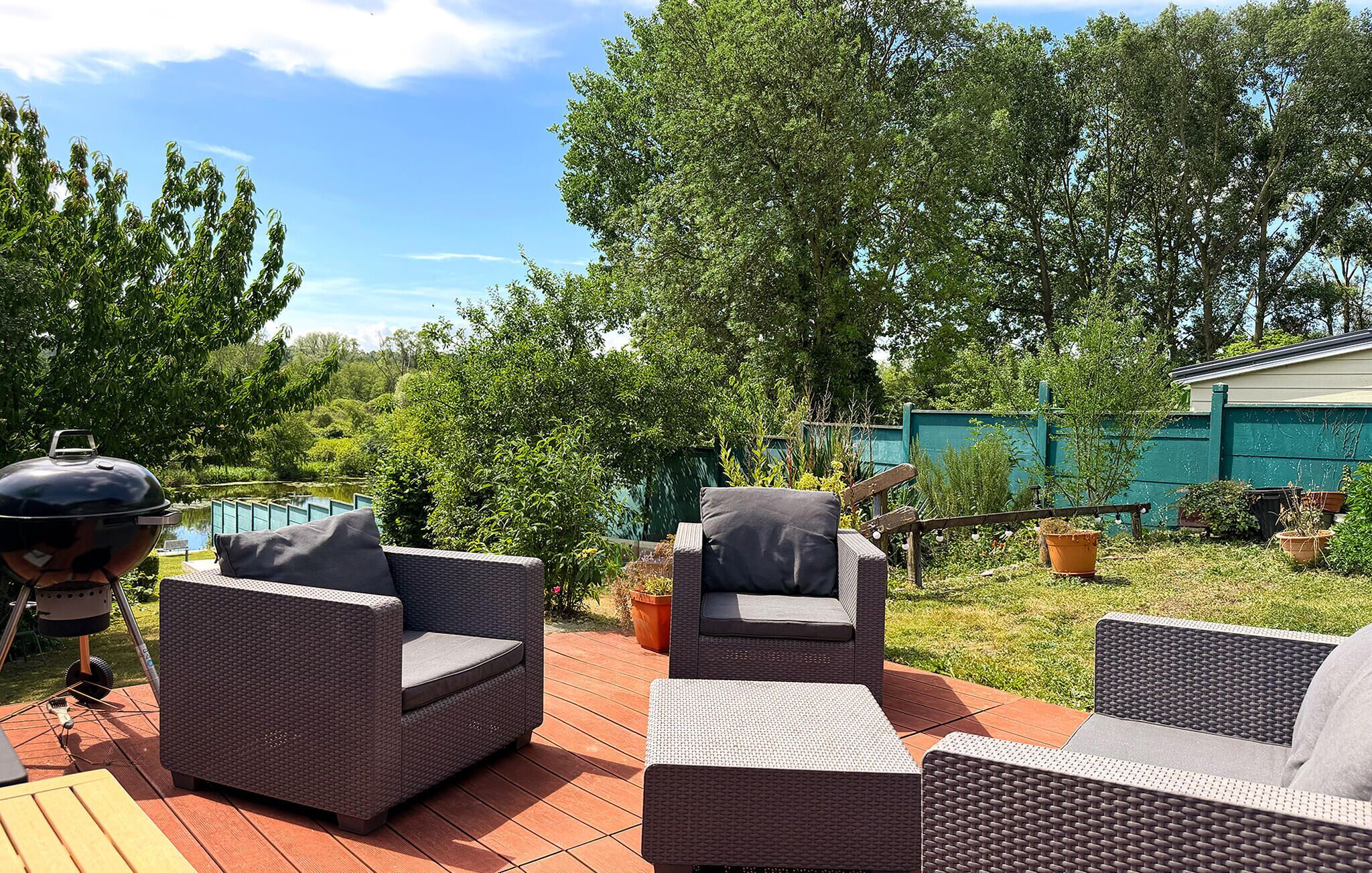 Een terras buiten met rieten meubilair, een barbecue en een zwembad op de achtergrond.