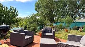 Een terras buiten met rieten meubilair, een barbecue en een zwembad op de achtergrond.