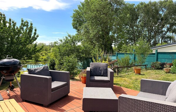 Un patio exterior con mobiliario de mimbre, una parrilla y una piscina al fondo.
