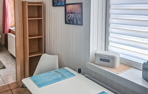 A room with a white table, a blue placemat, a wooden shelf, a radiator, and a window with blinds. - Gorgeous apartment in Kalkhorst (Kalkhorst)