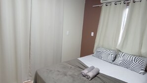 Ett sovrum med en säng, gardiner, en luftkonditioneringsanläggning och ett trägolv.