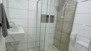 Ett modernt badrum med en dusch som är avskärmad med glasväggar, ett vitt handfat och en toalett.