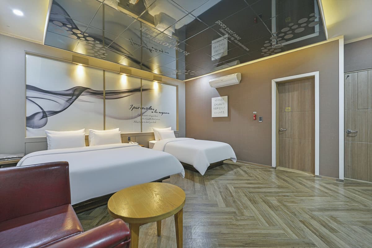 A hotel room with two beds, a red chair, a small round table, and a large abstract wall art piece.