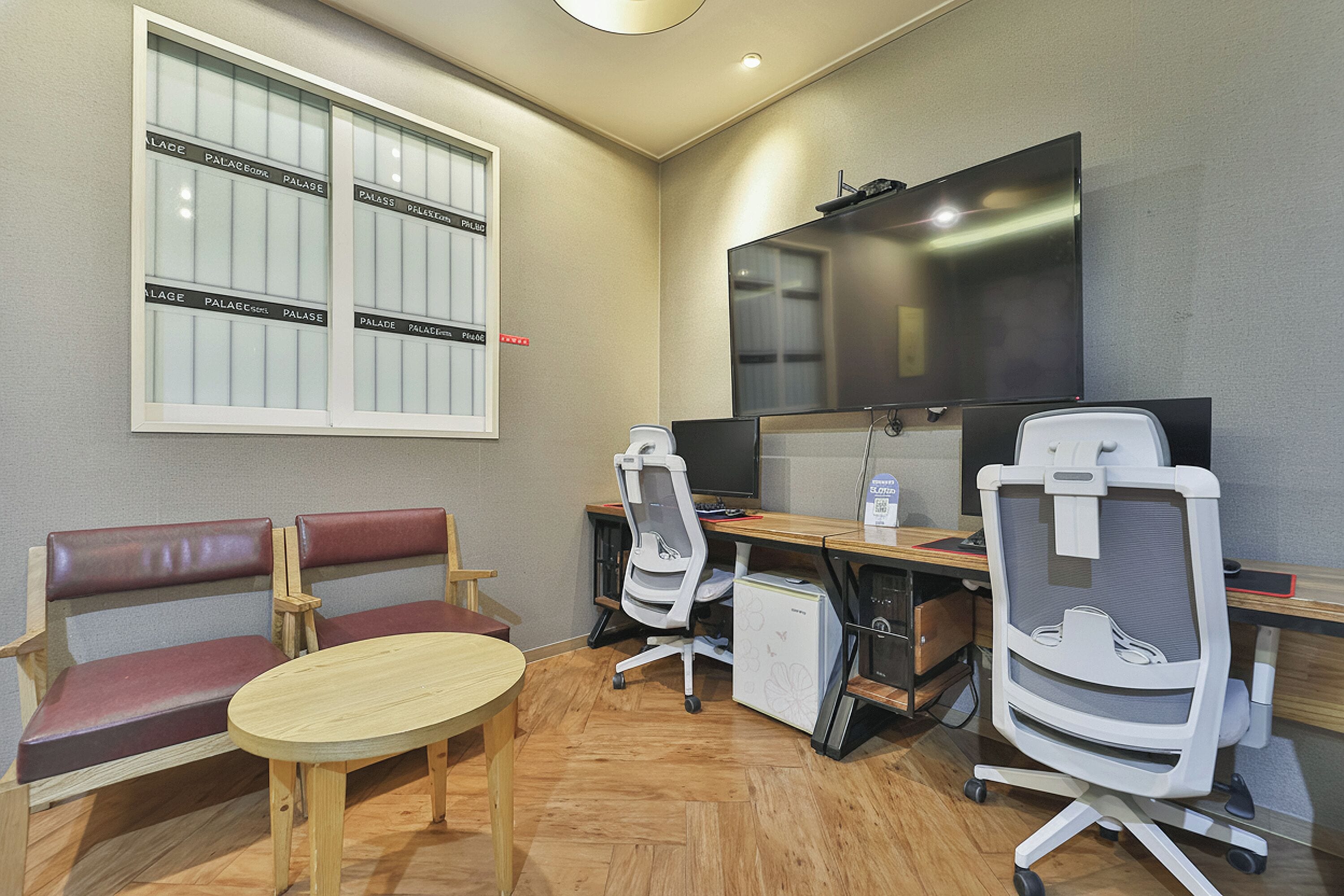 A conference room with a large TV, two office chairs, a wooden table, and a bench with red cushions.