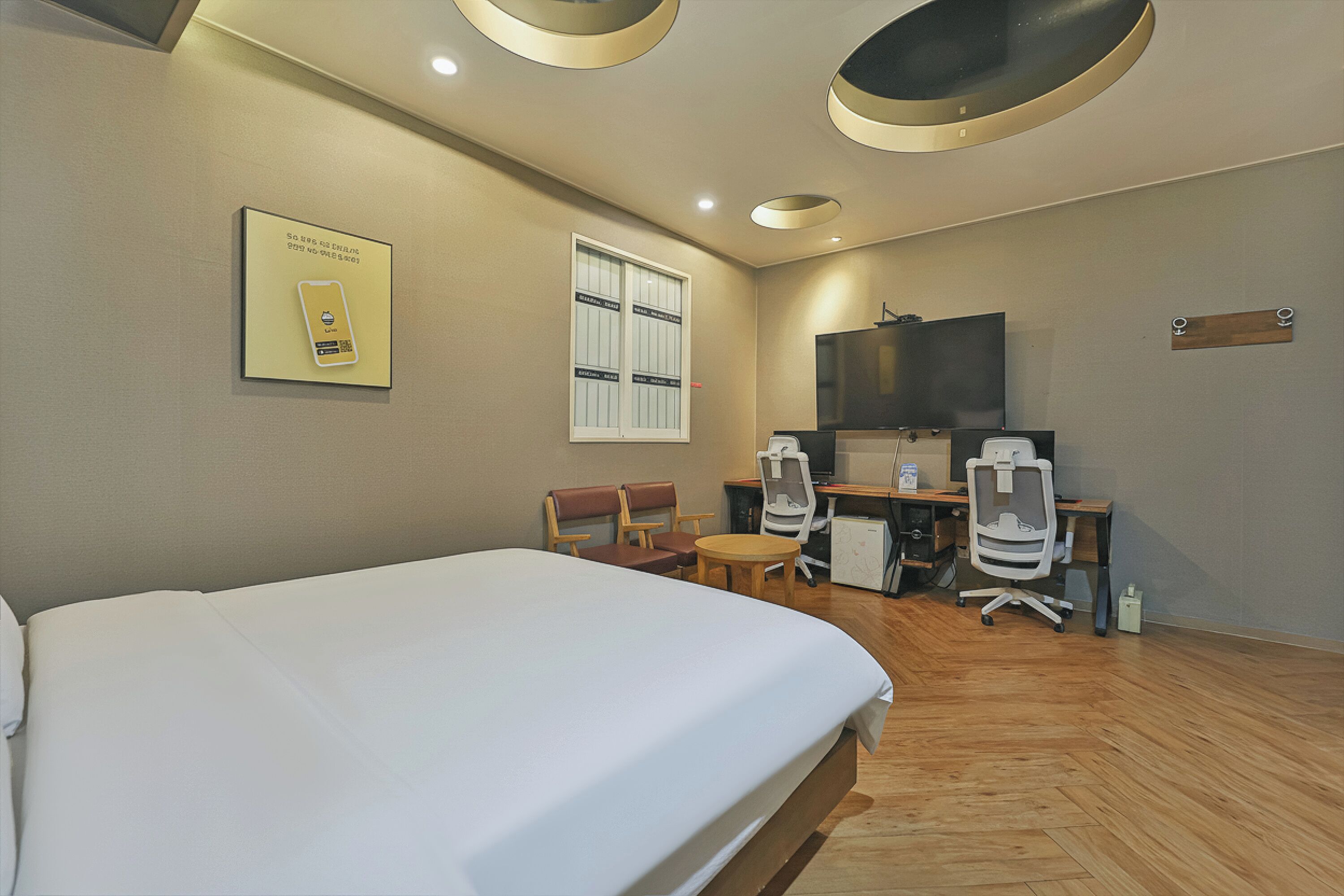 A hotel room with a bed, a desk, two chairs, a television, and a window.