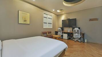 A hotel room with a bed, a desk, two chairs, a television, and a window.
