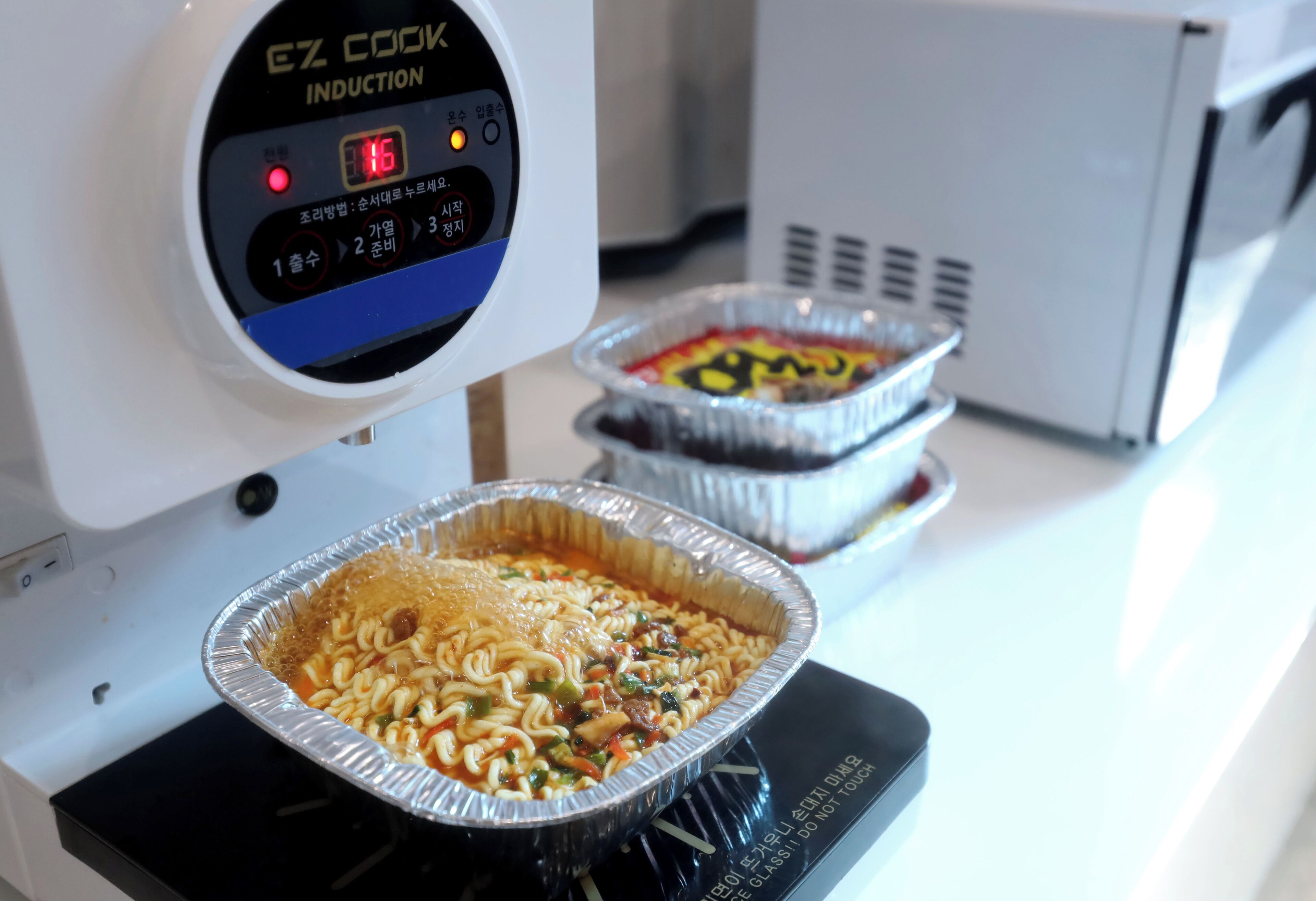 Una cocina con una placa de inducción y dos sartenes de aluminio encima.