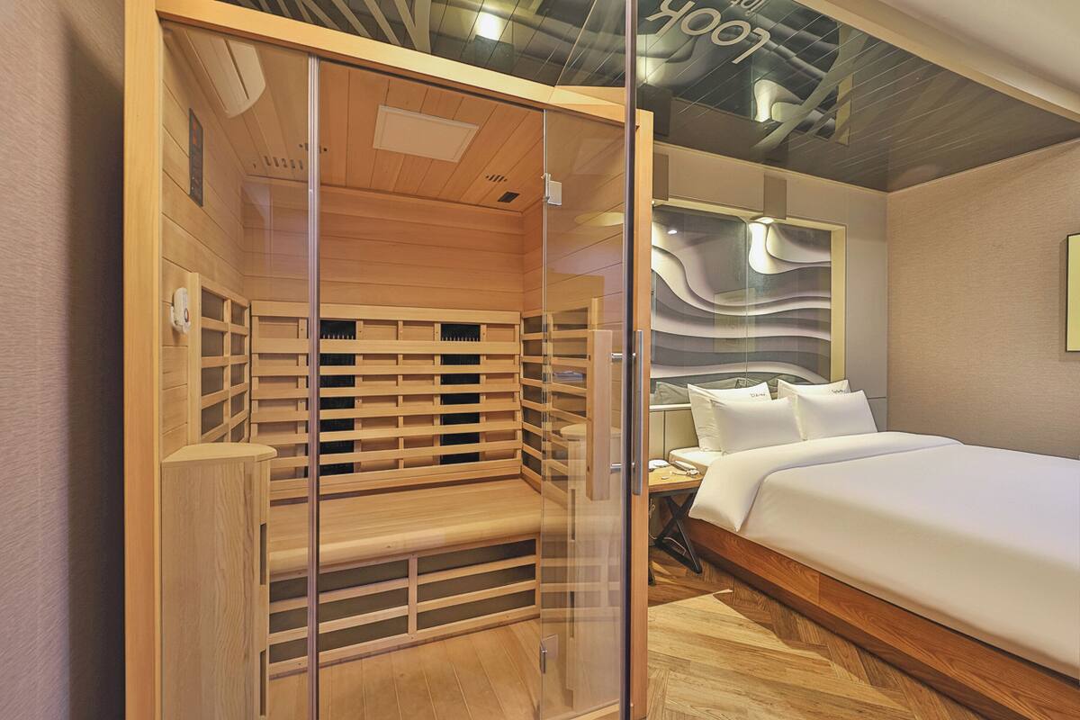 A modern hotel room with a wooden bench, a bed, and a glass partition.