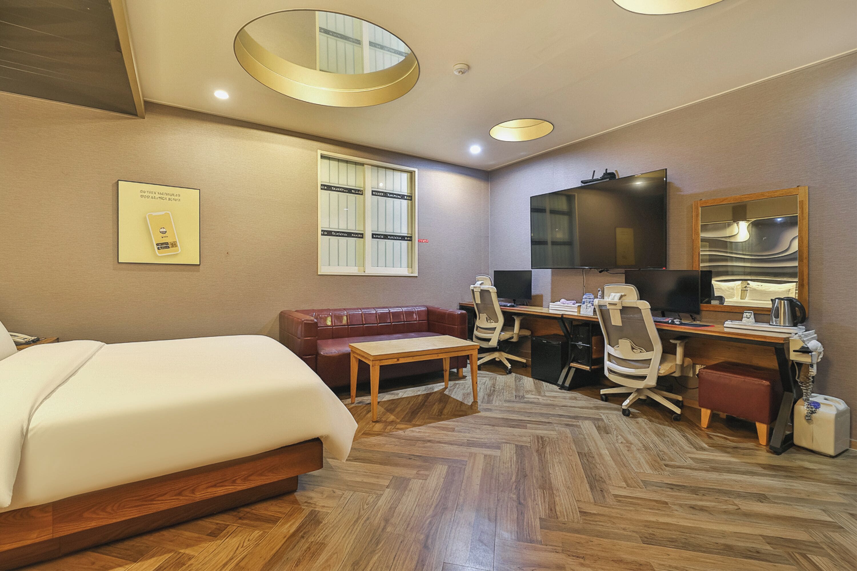 A hotel room with a bed, a desk with a computer, a chair, a sofa, and a television.