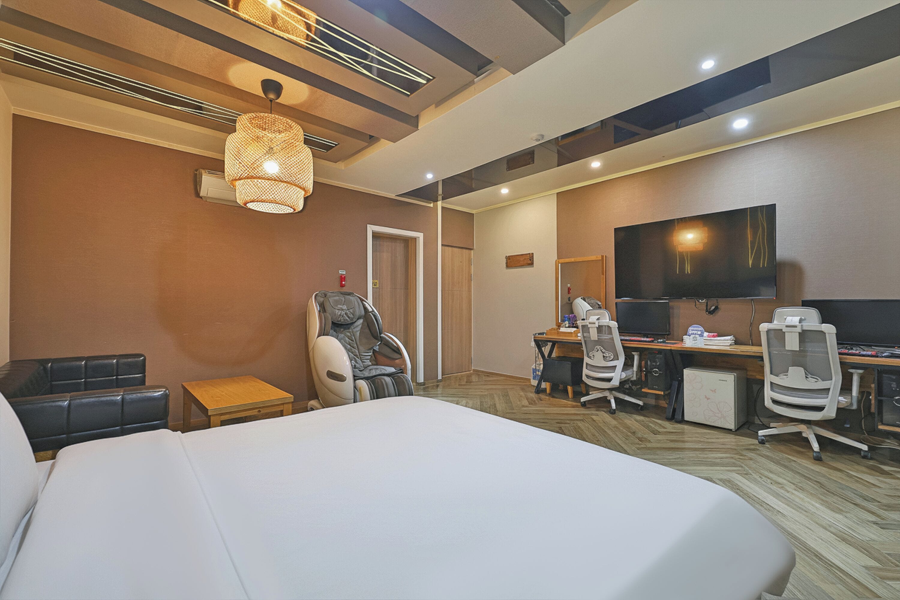 Quarto de hotel com uma cama grande, uma cadeira de massagem, uma escrivaninha com computador e uma televisão.