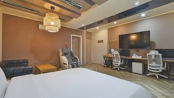 Quarto de hotel com uma cama grande, uma cadeira de massagem, uma escrivaninha com computador e uma televisão.