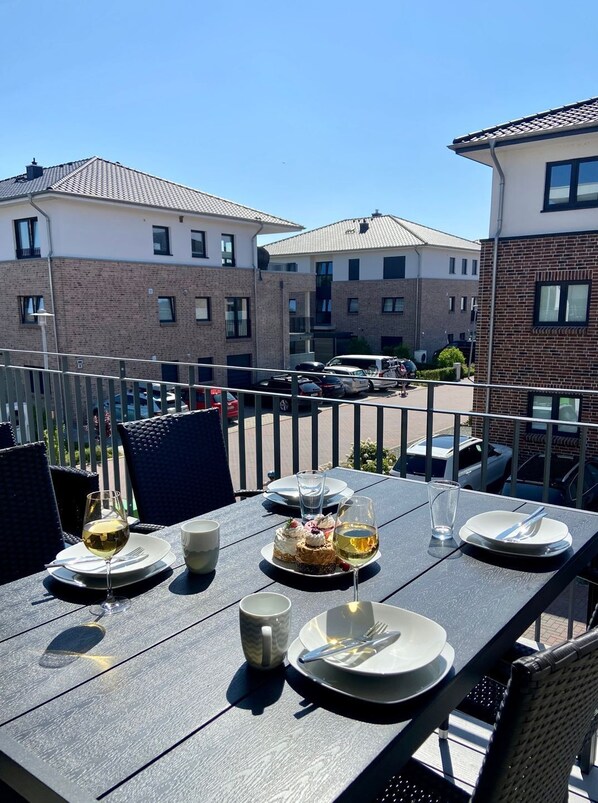 An outdoor dining area with tables set for two, chairs, and a view of residential buildings in the background.