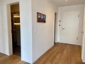 A hallway with wooden flooring, a white door, and a small framed picture on the wall.