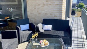 Un área de estar al aire libre con mobiliario de mimbre, una mesa de cristal y un plato de postres.