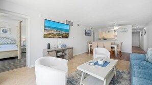 A modern living room with a TV, white furniture, a dining area, and a view of the beach. - La Mirage Condo 106 Beachfront Resort Condominiums with Private Boardwalk (Port Aransas)