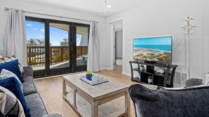Amplia sala de estar con un gran ventanal corredizo que da a un balcón, un televisor de pantalla plana sobre un soporte negro y una mesa de centro con adornos.