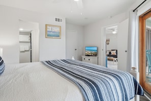 Un dormitorio con cama, televisor, un cuadro y una puerta que da a otra habitación.