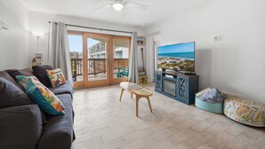 A living room with a sofa, a small table, a TV, and a view of the sea through a sliding door. - La Mirage Condo 218 Beachfront Resort Condominiums with Private Boardwalk (Port Aransas)