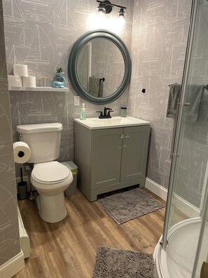A bathroom with a toilet, sink, and mirror, featuring a nautical-themed wallpaper.