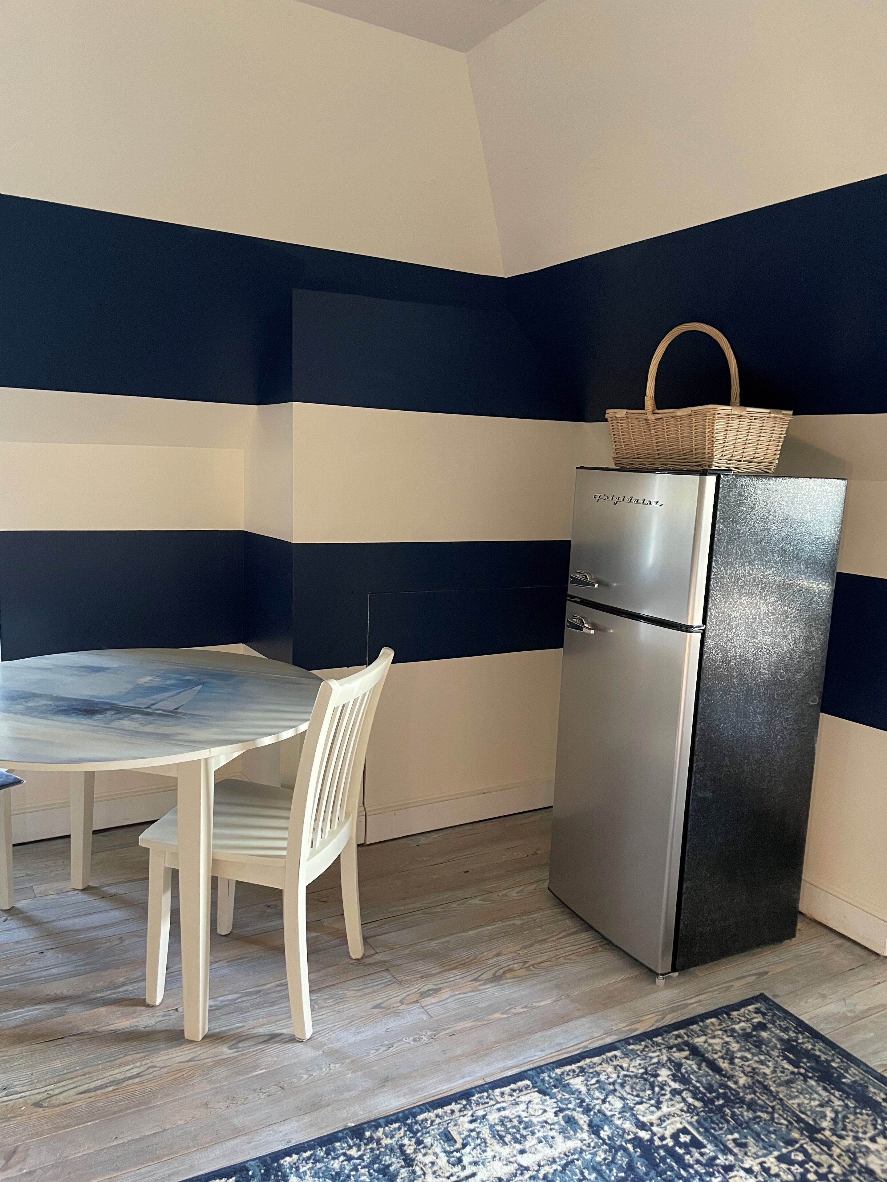 A compact kitchen with a dining table and chairs, a refrigerator, and a patterned rug.