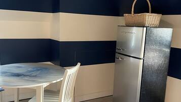 A compact kitchen with a dining table and chairs, a refrigerator, and a patterned rug.