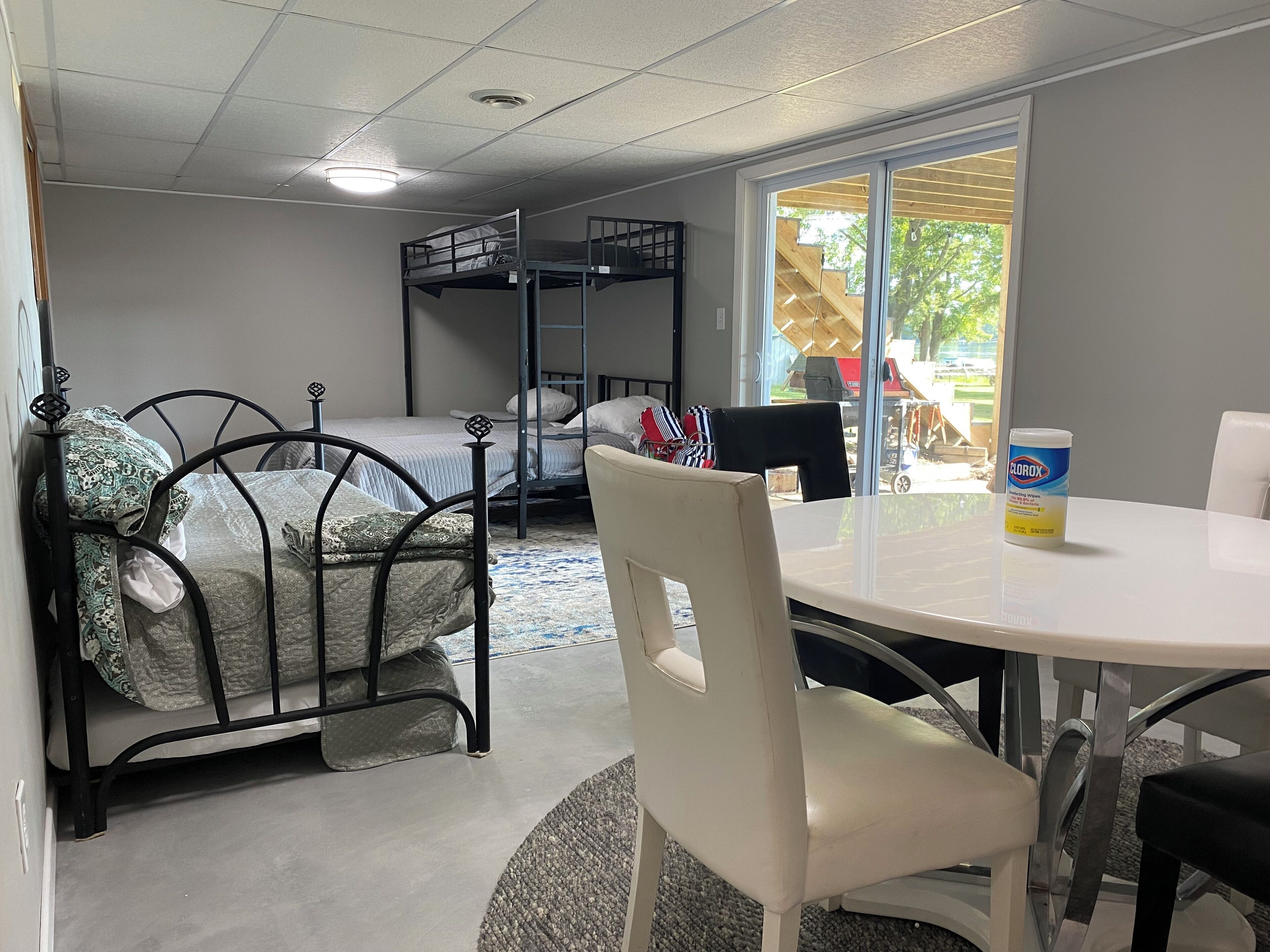A bunk bed with a metal frame, a round table with a chair, and a window with a view of the outside.
