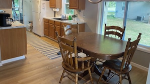 Een keuken met houten kastjes, een eettafel met stoelen, een kroonluchter en uitzicht op de achtertuin door een raam.