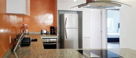 A modern kitchen with granite countertops, stainless steel appliances, and a glass ceiling light fixture.