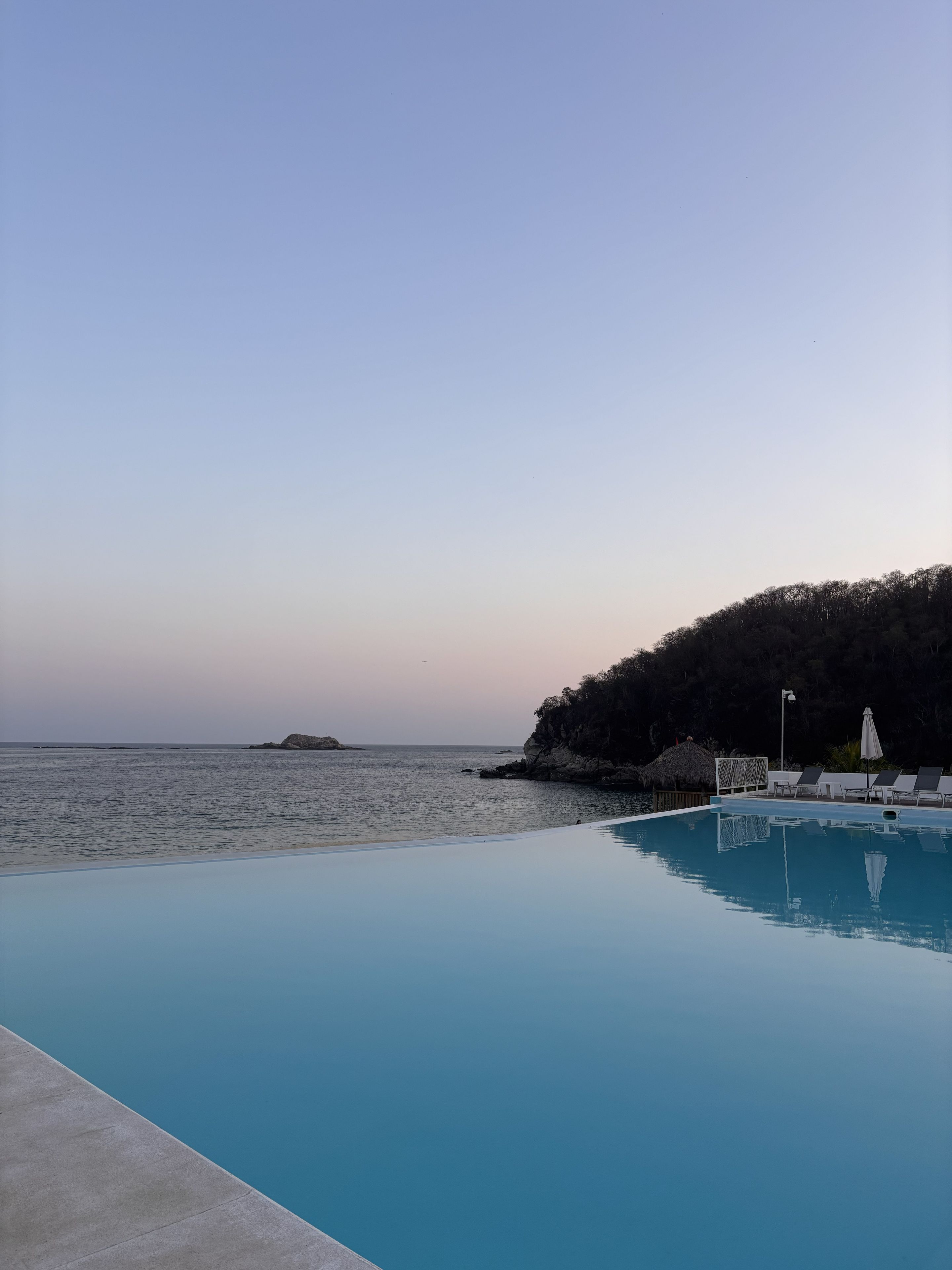 A clear sky, calm sea, and a swimming pool with lounge chairs.