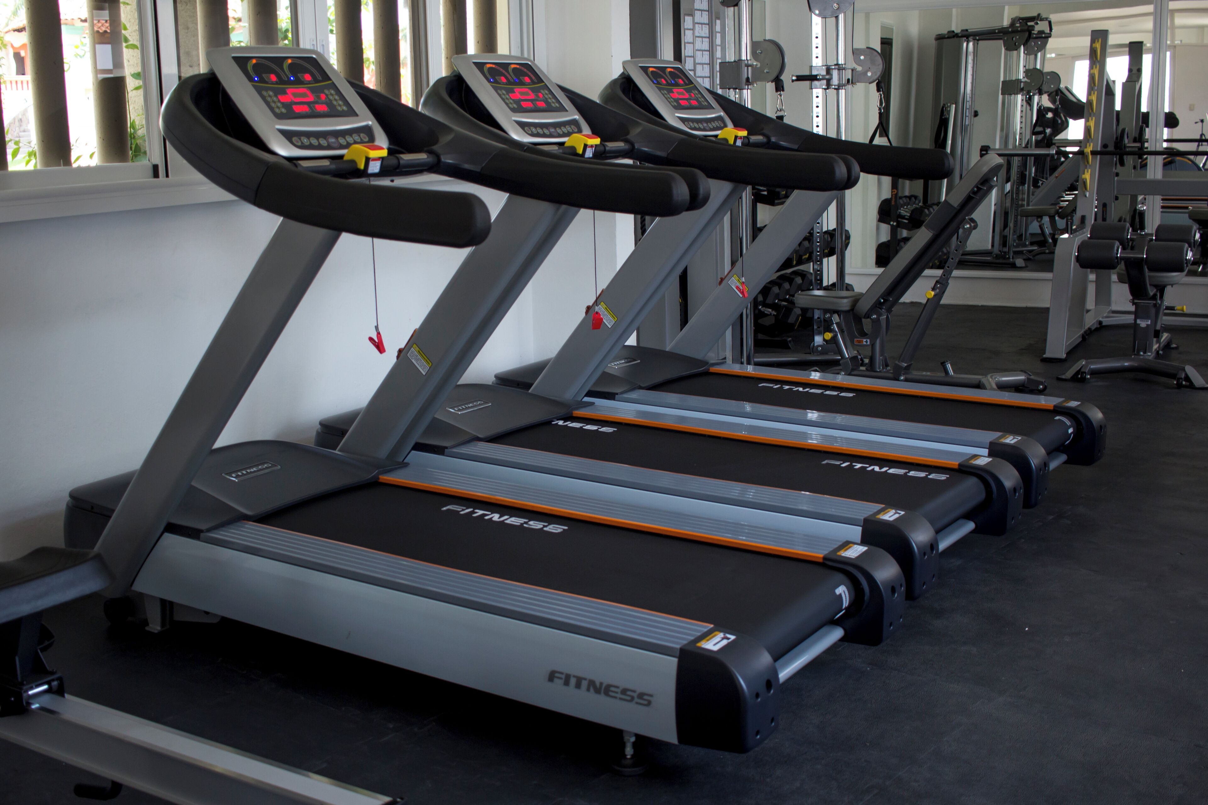 Three treadmill machines in a gym with mirrors and weightlifting equipment in the background.