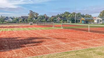 An outdoor tennis court with a net, surrounded by trees and buildings.
