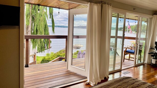 Ein Zimmer mit großen Schiebeglasfenstern, die auf eine Terrasse mit Blick auf einen See und eine Anlegestelle führen.