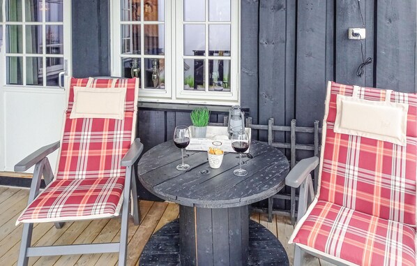A round wooden table with two chairs, each with a plaid cushion. There are two glasses of red wine on the table.