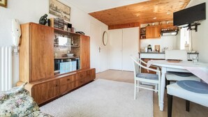 Ein kompakter Wohnraum mit einem Holzschrank, einem Esstisch mit Stühlen, einer Küchenzeile und einer weißen Heizkörper.