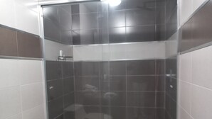 A small, enclosed shower area with a glass door, a toilet, and a sink. - Loft Shandde Park (Quito)