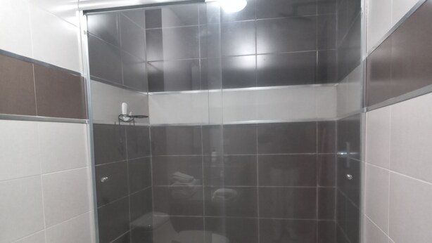 A small, enclosed shower area with a glass door, a toilet, and a sink. - Loft Shandde Park (Quito)