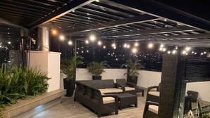 An outdoor patio area with a sofa set, potted plants, and string lights. - Loft Shandde Park (Quito)