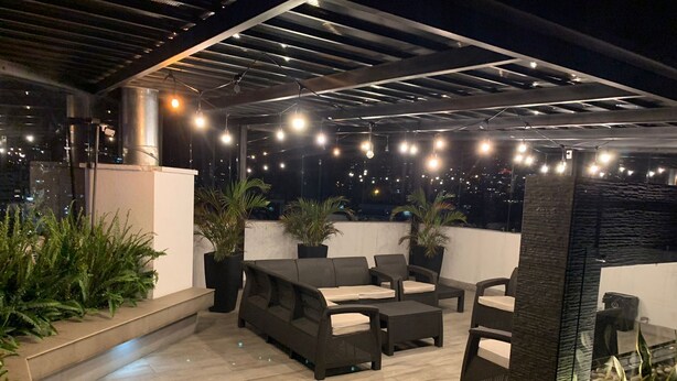 An outdoor patio area with a sofa set, potted plants, and string lights. - Loft Shandde Park (Quito)