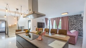 Une cuisine moderne avec un îlot central, un coin repas avec six chaises, un canapé rose et un mur en pierre.