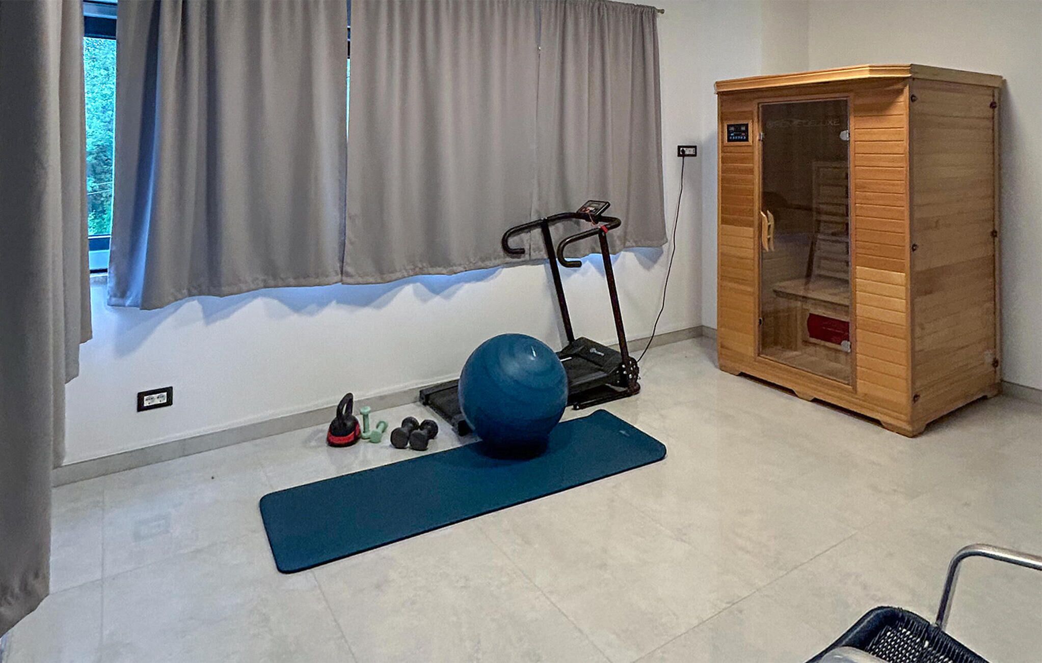Quarto com sauna de madeira, bola de exercícios azul e esteira.
