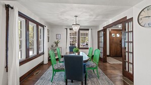 Un coin repas avec une table ronde, des chaises vertes, un lustre et une horloge au mur.
