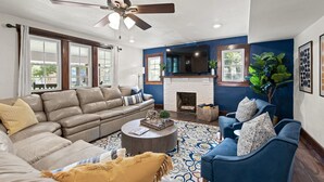 Un salon comprenant un canapé d’angle, un fauteuil bleu, une cheminée et un ventilateur de plafond.
