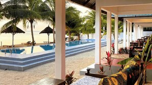 Un espace piscine situé au bord de la plage, avec un fauteuil de relaxation, une table et une vue sur la plage et l’océan.